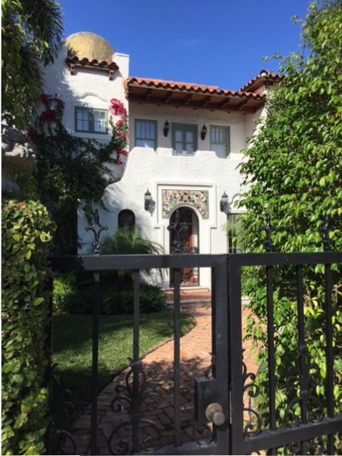 A broken tile pediment and iron door personalize the entry of this Spanish-style home also in Palm Beach.