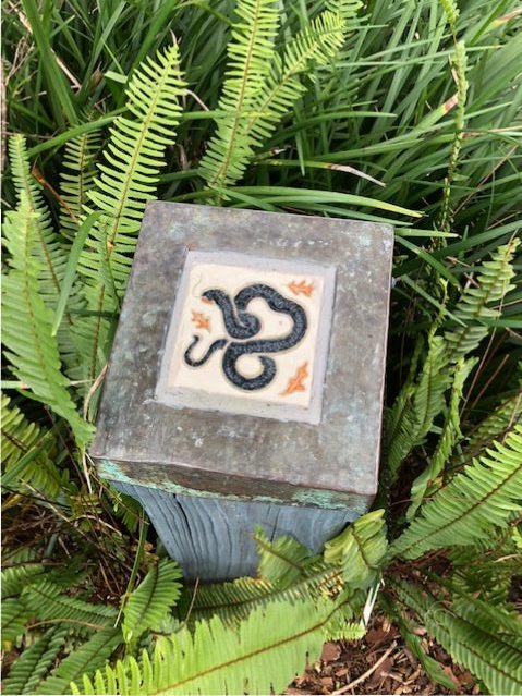 A cute snake tile is tucked into a bed of ferns, Bok Tower and Gardens.